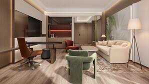 A modern hotel room with a wooden floor, a dining table, a sofa, a green armchair, a red accent wall, and a large window.