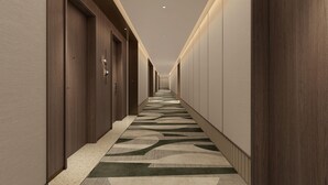 A long, narrow hotel corridor with wooden doors, recessed lighting, and patterned carpet.