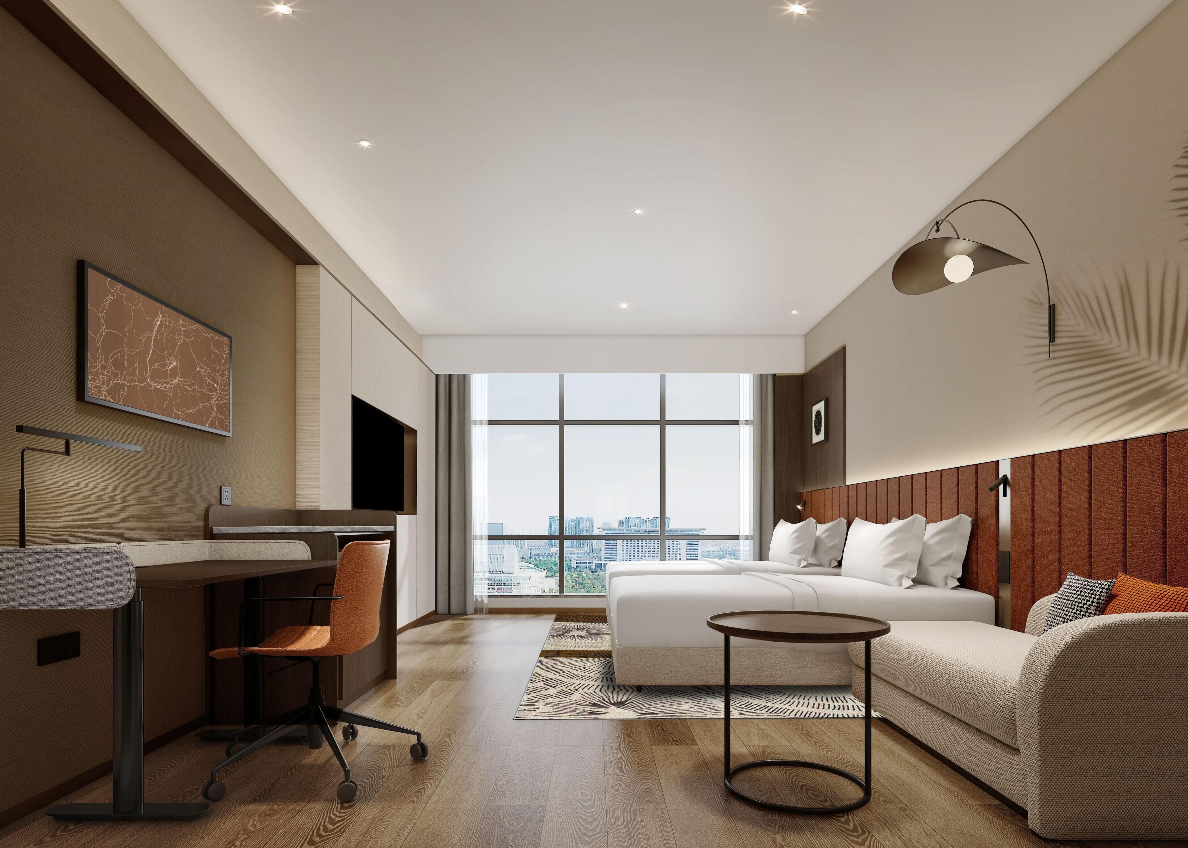 A modern hotel room with a bed, desk, chair, and a large window offering a city view.
