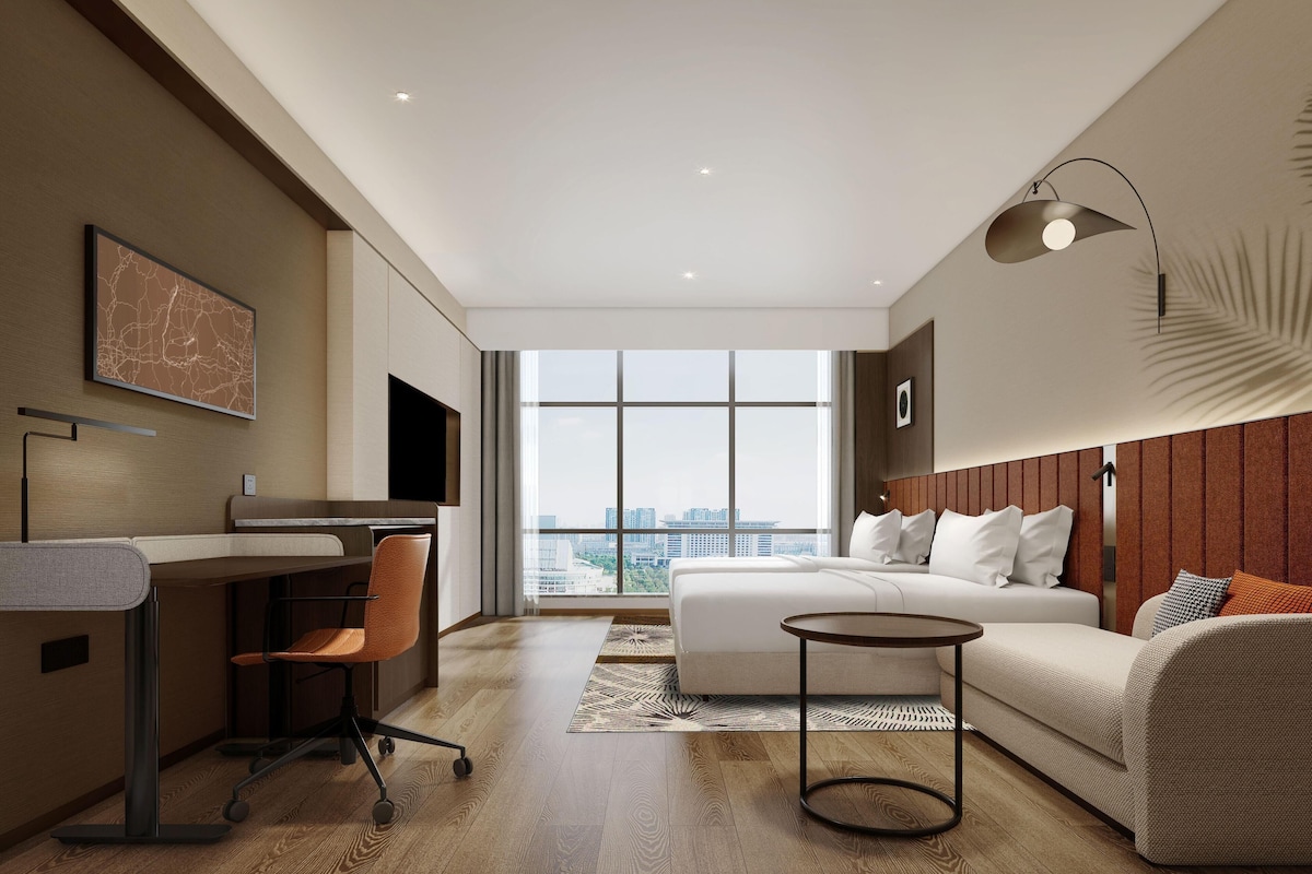 Una habitación de hotel moderna con cama, escritorio, silla y un ventanal con vistas a la ciudad.