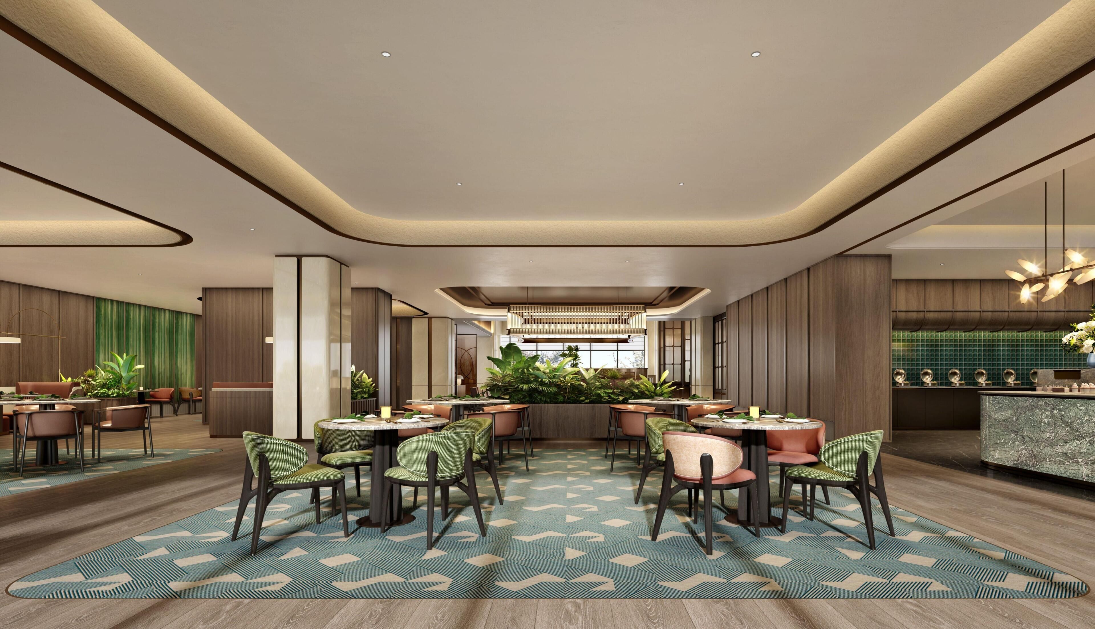 A modern hotel lobby with round tables, green chairs, a patterned rug, and a central plant arrangement.