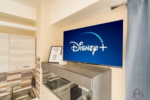 Een moderne keuken met een flatscreen-tv waarop het Disney+ logo staat, een ingelijst welkomstbord en een keukenblad met glazen voorzetstuk.