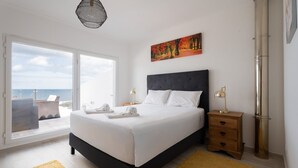 Ein Schlafzimmer mit einem großen Bett, einem Nachttisch, einer Lampe, einem Gemälde und Meerblick.