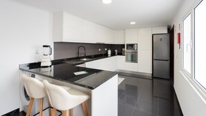 Eine moderne Küche mit einer zentralen Kochinsel, weißen Schränken, einem eingebauten Backofen und einem Edelstahl-Kühlschrank.