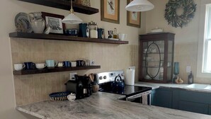 Una cocina con isla de mármol, dos taburetes de bar, una estufa y diversos utensilios de cocina en estantes.