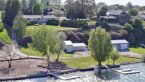 A lakeside property with a dock, a small building, and a large house in the background.