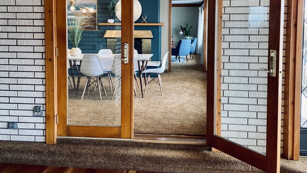 A room with wooden flooring, a brick wall, and a sliding glass door leading to a dining area with chairs and a table.