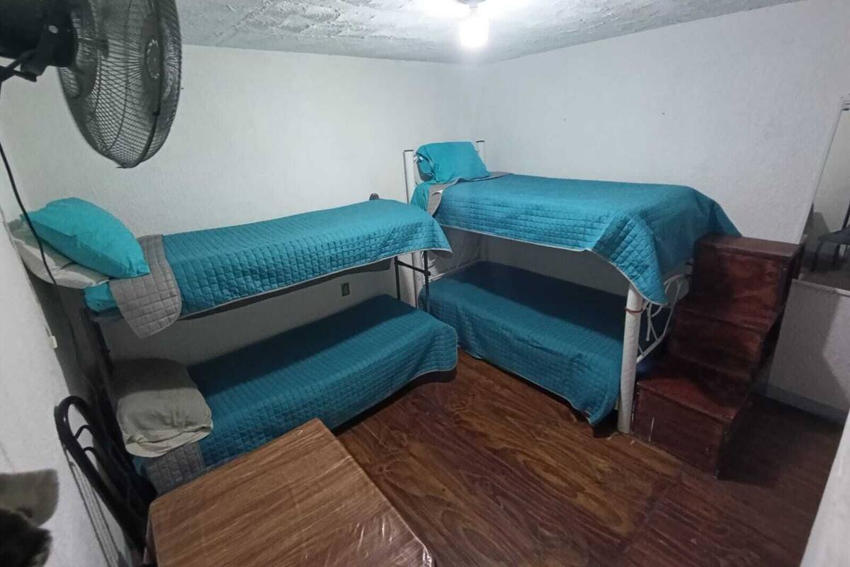 Ein kleiner, kompakter Raum mit Etagenbetten, einem Ventilator und Holzboden.