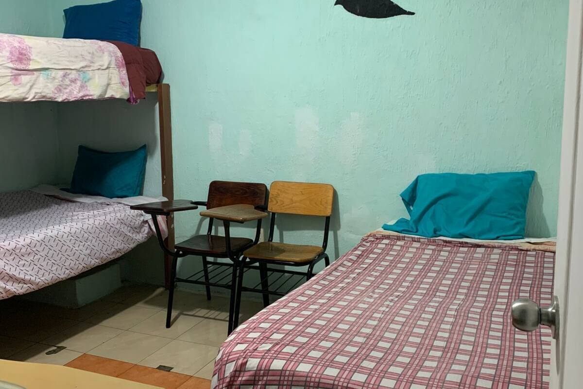 Ein Schlafsaalzimmer mit Etagenbetten, einem Schreibtisch, Stühlen und Wandmalerei.