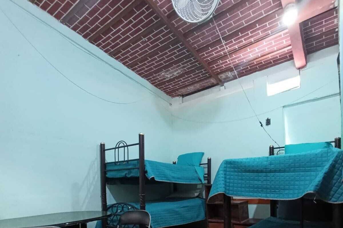 Ein Schlafsaalzimmer mit Etagenbetten, einem Schreibtisch, einem Stuhl und einem Deckenventilator.