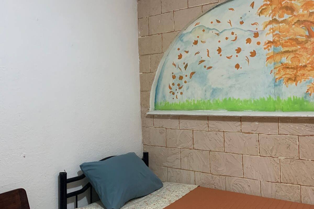 Ein Schlafzimmer mit Bett, Stuhl, Tisch und Wandgemälde.