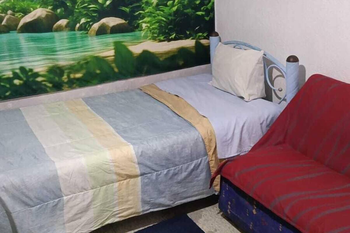 Ein Schlafzimmer mit einem Bett, einem roten Sofa, einem Wandgemälde mit einer tropischen Szene und einem Fenster.