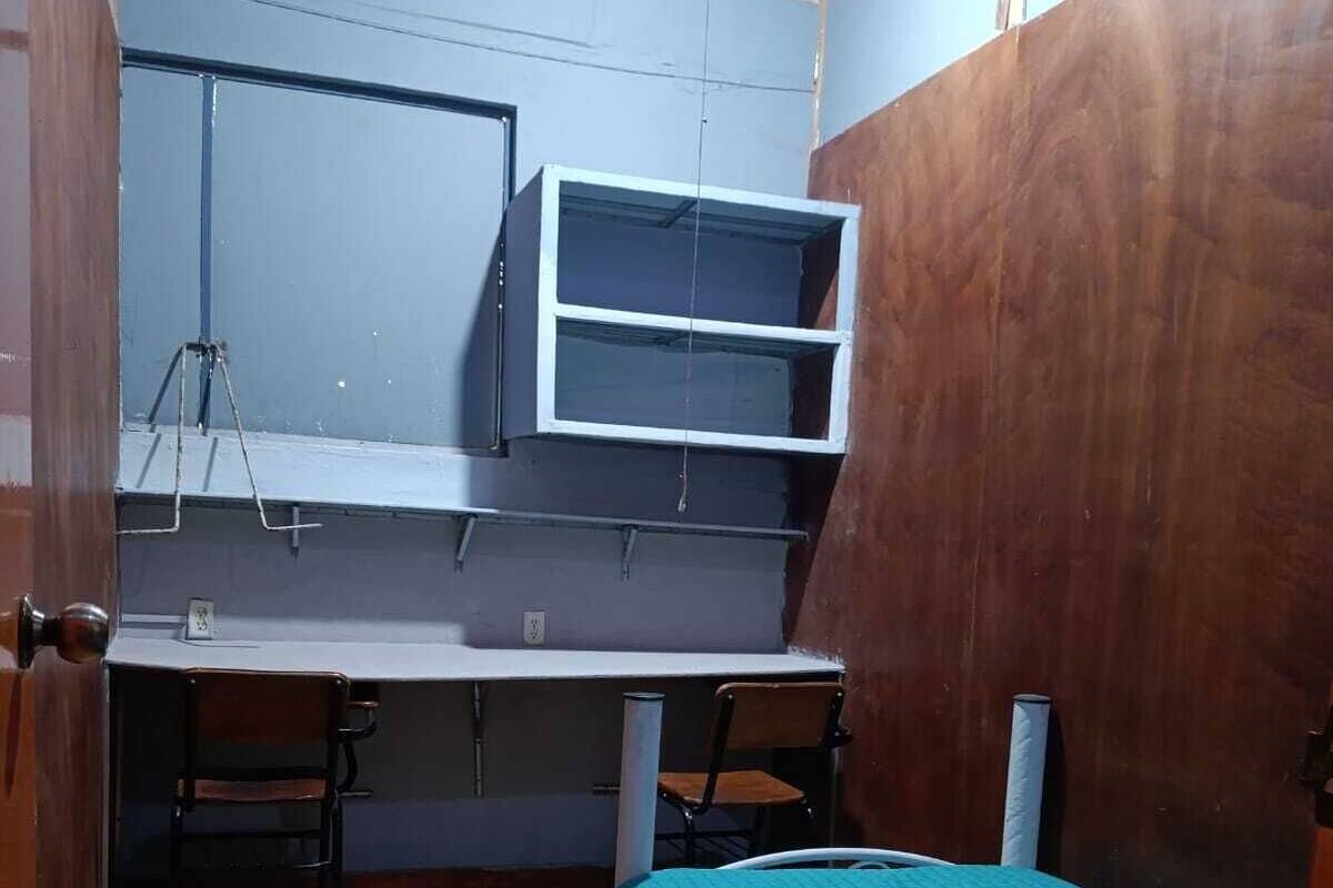 Ein kleiner, kompakter Raum mit Holzboden, einem Bett mit türkisfarbenem Überwurf, einem Schreibtisch mit Computer und einem Stuhl.