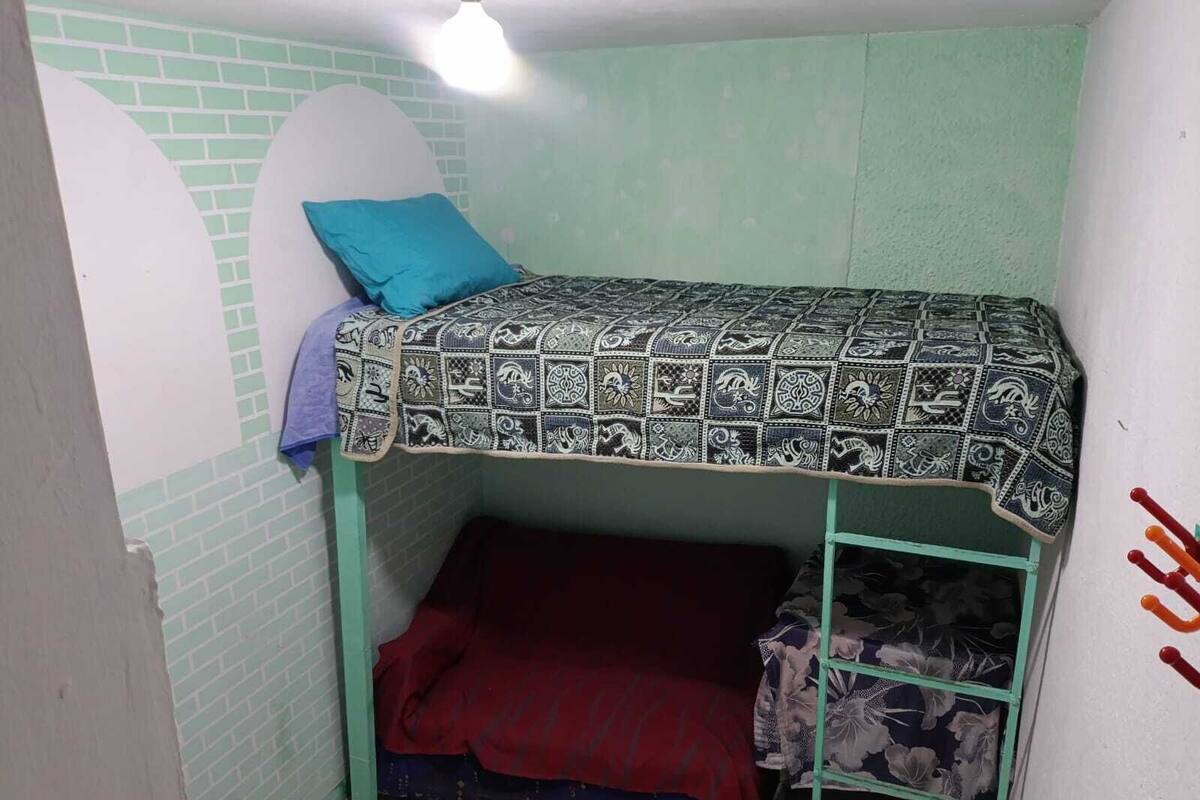 Ein Stockbett mit einem gemusterten Bettüberwurf, einem blauen Kopfkissen und einer roten Decke.