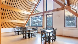 A spacious room with a high ceiling and large windows, featuring a wooden beam structure and a dining area with chairs and tables. - Mountain Lodging With Private Balcony (Saint-Colomban-des-Villards)