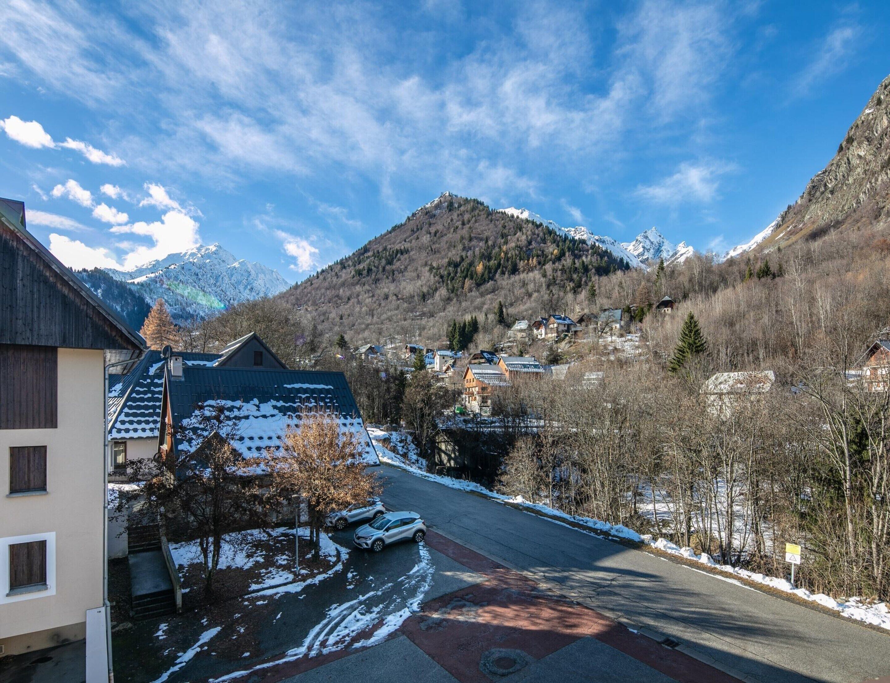A mountain village with snow-covered streets and houses, a clear sky, and a view of snow-capped mountains.