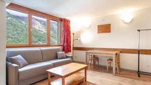 Una stanza con un divano, un tavolo in legno, un'area pranzo e vista su un paesaggio montuoso attraverso ampie finestre.