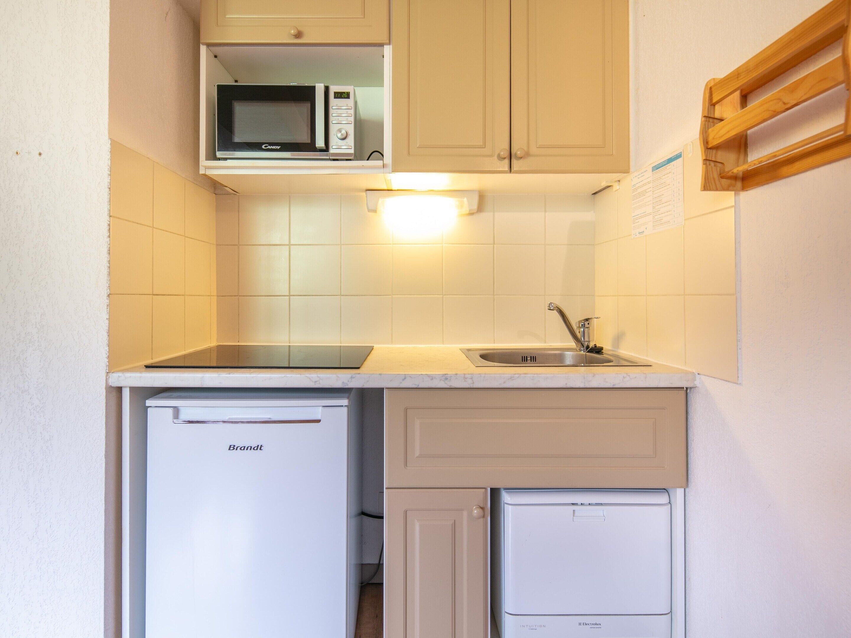Una cocina funcional equipada con microondas, lavamanos y un refrigerador pequeño.