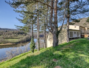 Ett hus med utsikt över floden, omgivet av träd och en gräsyta.