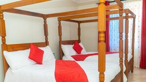 Una cama con dosel, ropa de cama blanca y roja, cabecera de madera y cortinas.
