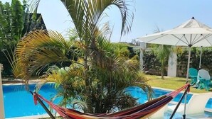Un patio con una hamaca, una piscina y mobiliario exterior.