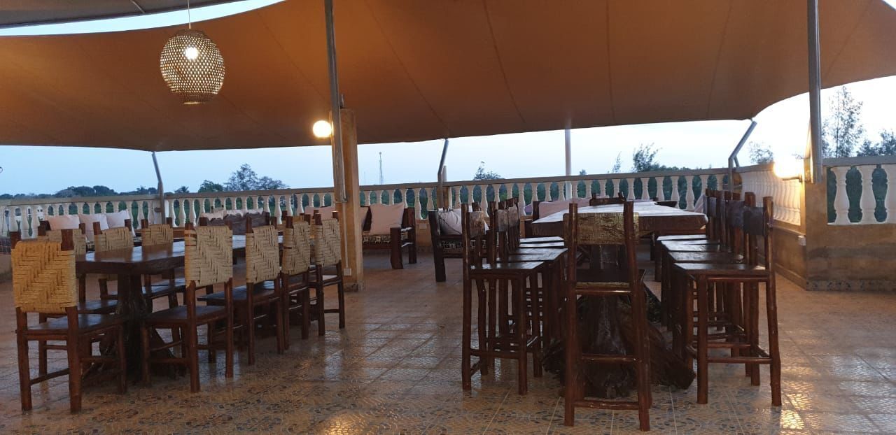 An outdoor dining area with wooden tables and chairs, a large umbrella, and a decorative hanging light fixture.