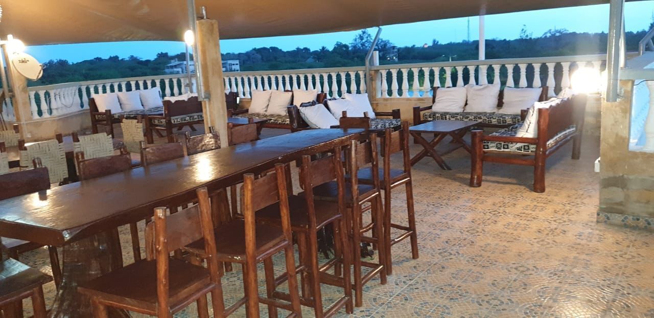 Une terrasse extérieure aménagée avec du mobilier en bois, notamment des tables et des chaises, située sous une zone abritée.
