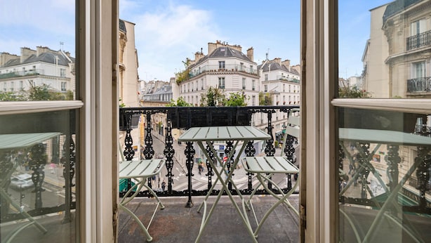 A balcony with a table and chairs, overlooking a street with buildings. - Gourmandise, 2BR/1BA, 4 people (Paris)