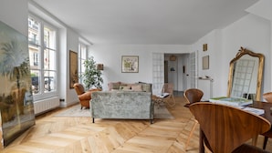 A spacious room with a herringbone wooden floor, a sofa, a dining table with chairs, and a large mirror. - Gourmandise, 2BR/1BA, 4 people (Paris)