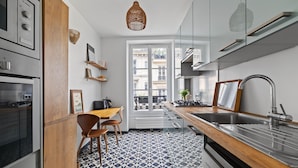 A modern kitchen with a geometric tile floor, wooden accents, and a view of the city through a large window. - Gourmandise, 2BR/1BA, 4 people (Paris)