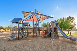 A playground with slides and climbing structures, surrounded by a gravel area and trees. - Paradise Village Resort 31/32 Retreat (Santa Clara)