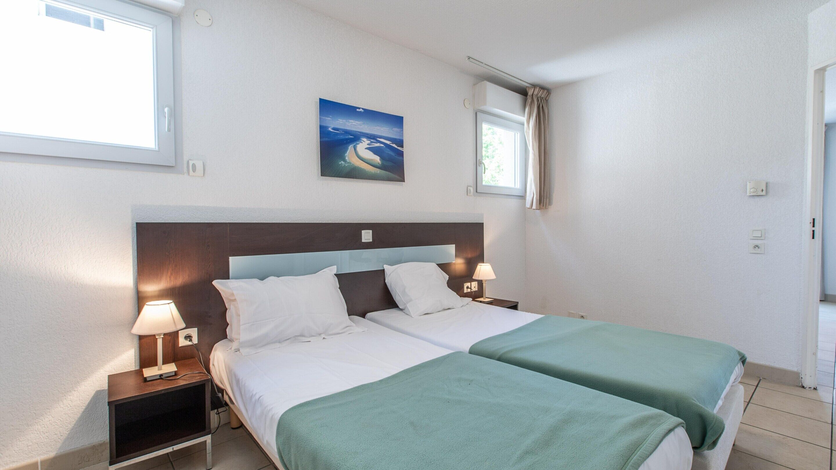 Habitación de hotel con cama doble, dos mesitas de noche con lámparas, un cuadro en la pared y una ventana con cortinas.
