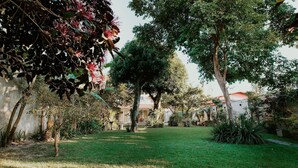 A garden with trees, a lawn, and a building with a red roof. - Cozy House with Gourmet Area and Pool (Vila Velha)
