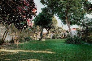 A garden with trees, a lawn, and a building with a red roof. - Cozy House with Gourmet Area and Pool (Vila Velha)