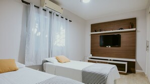 A hotel room with two beds, a TV, and a wooden shelf with decorative items. - Cozy House with Gourmet Area and Pool (Vila Velha)
