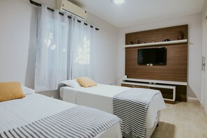 A hotel room with two beds, a TV, and a wooden shelf with decorative items. - Cozy House with Gourmet Area and Pool (Vila Velha)