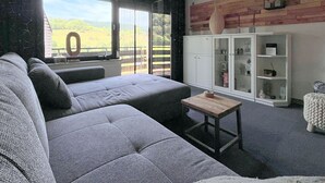 En moderne stue med en grå hjørnesofa, et lille træbord og et hvidt skab med glasdøre.