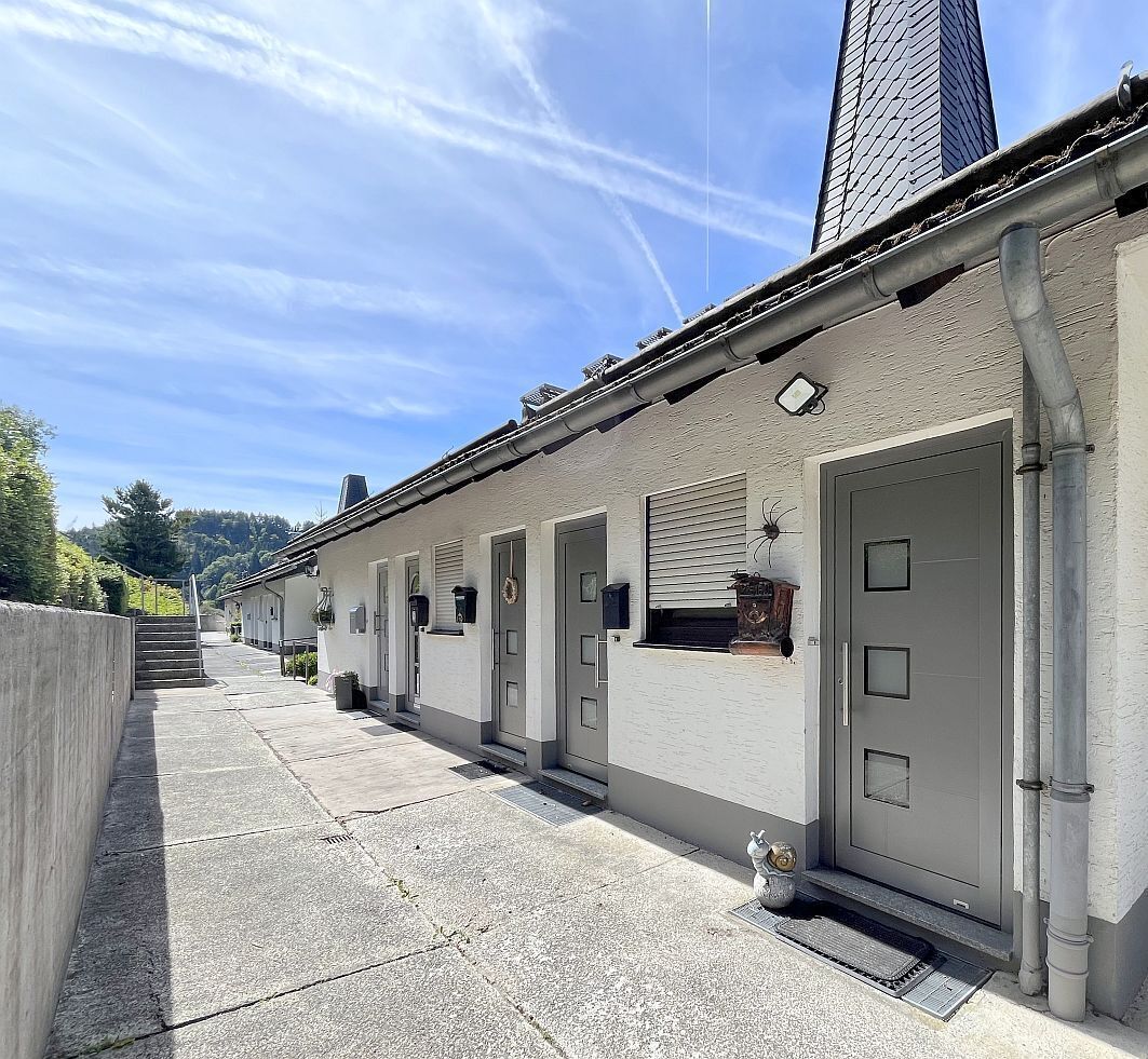 Eine Reihe eingeschossiger Gebäude mit grauen Türen, einem Betonweg und blauem Himmel.