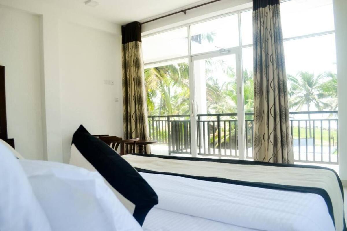 A hotel room with a bed, a chair, and a balcony with a view of palm trees.