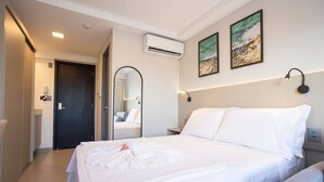 Ett hotellrum med en säng, en spegel, en luftkonditionering och konstverk på väggen.