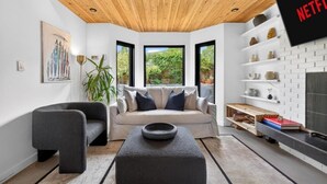 A modern living room with a sofa, armchair, and ottoman, a television, and a bookshelf. - Stylish 2BR/2BA |Large Private Patio|Near Downtown (Vancouver)