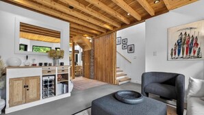 A modern interior with a wooden ceiling, a white wall with a framed painting, a grey sofa, and a wooden cabinet with wine racks. - Stylish 2BR/2BA |Large Private Patio|Near Downtown (Vancouver)