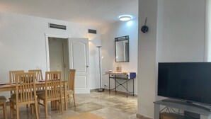 Ett vardagsrum med en TV, ett matbord med stolar, en golvlampa och en spegel på väggen.