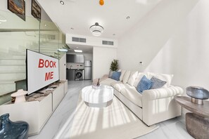 A modern living room with a sofa, coffee table, and a TV on a stand. - Free Housekeeping Visits During Your Stay - Stayshort - Cozy 1BR Townhouse Loft Style Located in Rukan Community (Dubai)
