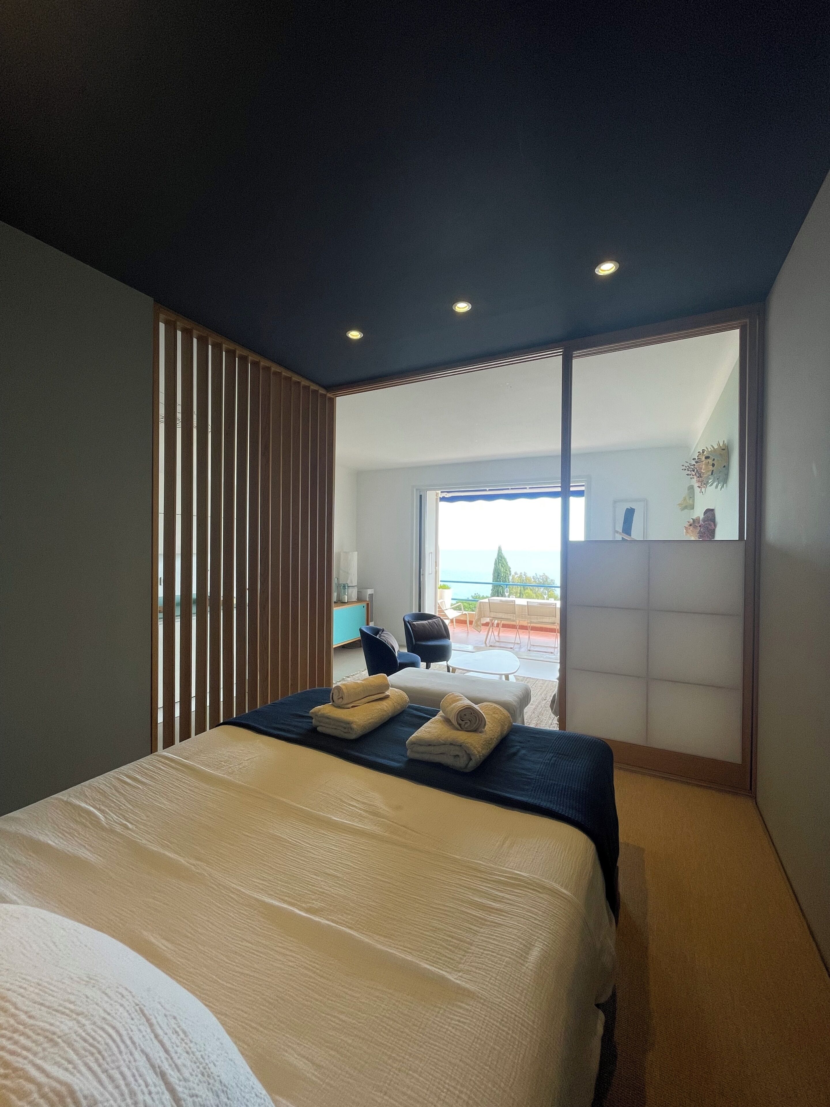 A modern bedroom with a bed, a view of the outdoors, and a sliding door leading to a balcony.