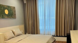 Una habitación de hotel con cama, escritorio, radiador y ventana con cortinas.