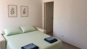Un dormitorio con una cama, dos almohadas, una puerta y dos diseños de hojas enmarcados en la pared.