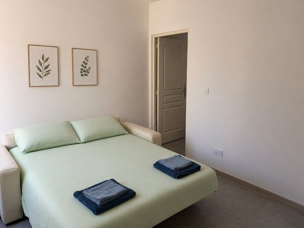 Un dormitorio con una cama, dos almohadas, una puerta y dos diseños de hojas enmarcados en la pared.
