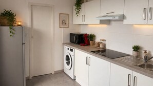 Una cocina moderna con armarios blancos, lavadora integrada, cafetera y lavabo.