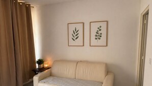 Una habitación con sofá, cortinas, una mesita con una planta e ilustraciones botánicas enmarcadas en la pared.